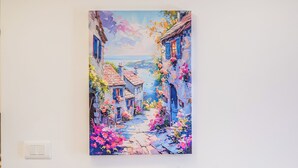 Um armário de madeira com uma pintura de uma cena urbana, uma pequena planta e alguns livros na prateleira.