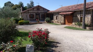 Une maison traditionnelle à colombages, avec une allée gravillonnée et un jardin agrémenté de fleurs rouges.