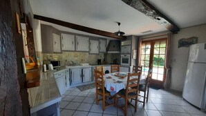 Une cuisine avec des meubles blancs, une table à manger avec des chaises, un réfrigérateur et une fenêtre avec des rideaux.
