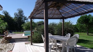 Une terrasse en bois avec un espace patio couvert, une piscine et une végétation luxuriante tout autour.