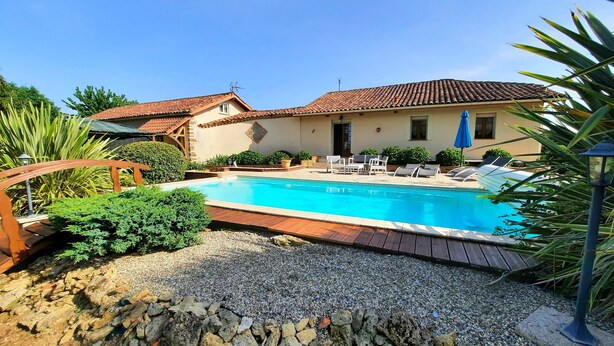Une piscine dotée d’une terrasse carrelée, entourée d’un mur de pierre et de verdure.