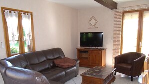 Un salon avec un canapé en cuir, une table basse en bois, un téléviseur posé sur un meuble en bois et un mur en briques.