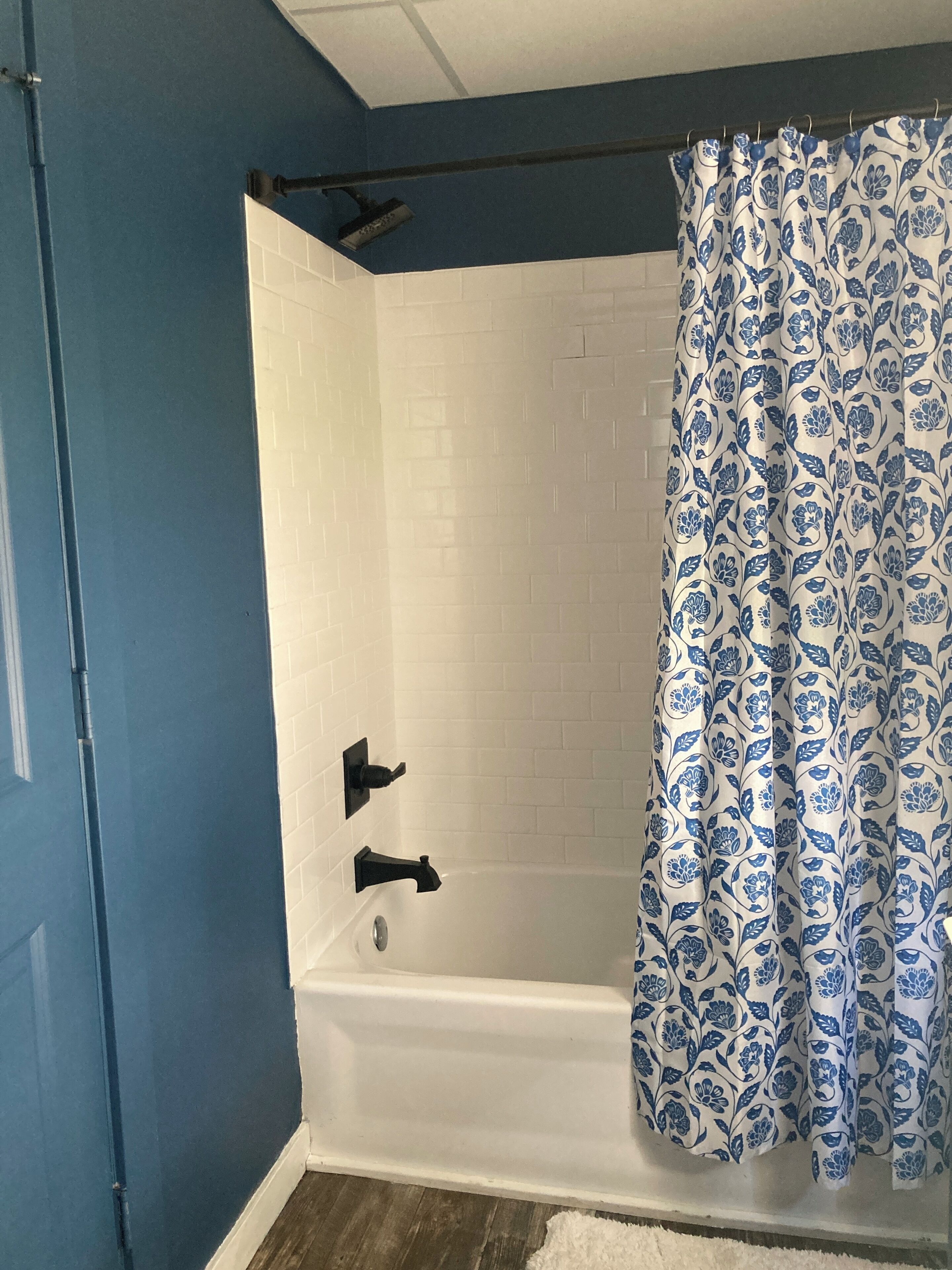 A bathroom with a white bathtub, blue walls, and a shower curtain with a blue floral pattern.