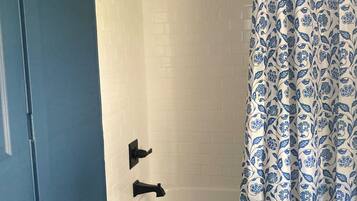 A bathroom with a white bathtub, blue walls, and a shower curtain with a blue floral pattern.