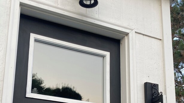 A dark-colored door with a window above it, a wall-mounted light fixture, and a 'WELCOME' sign on the right.
