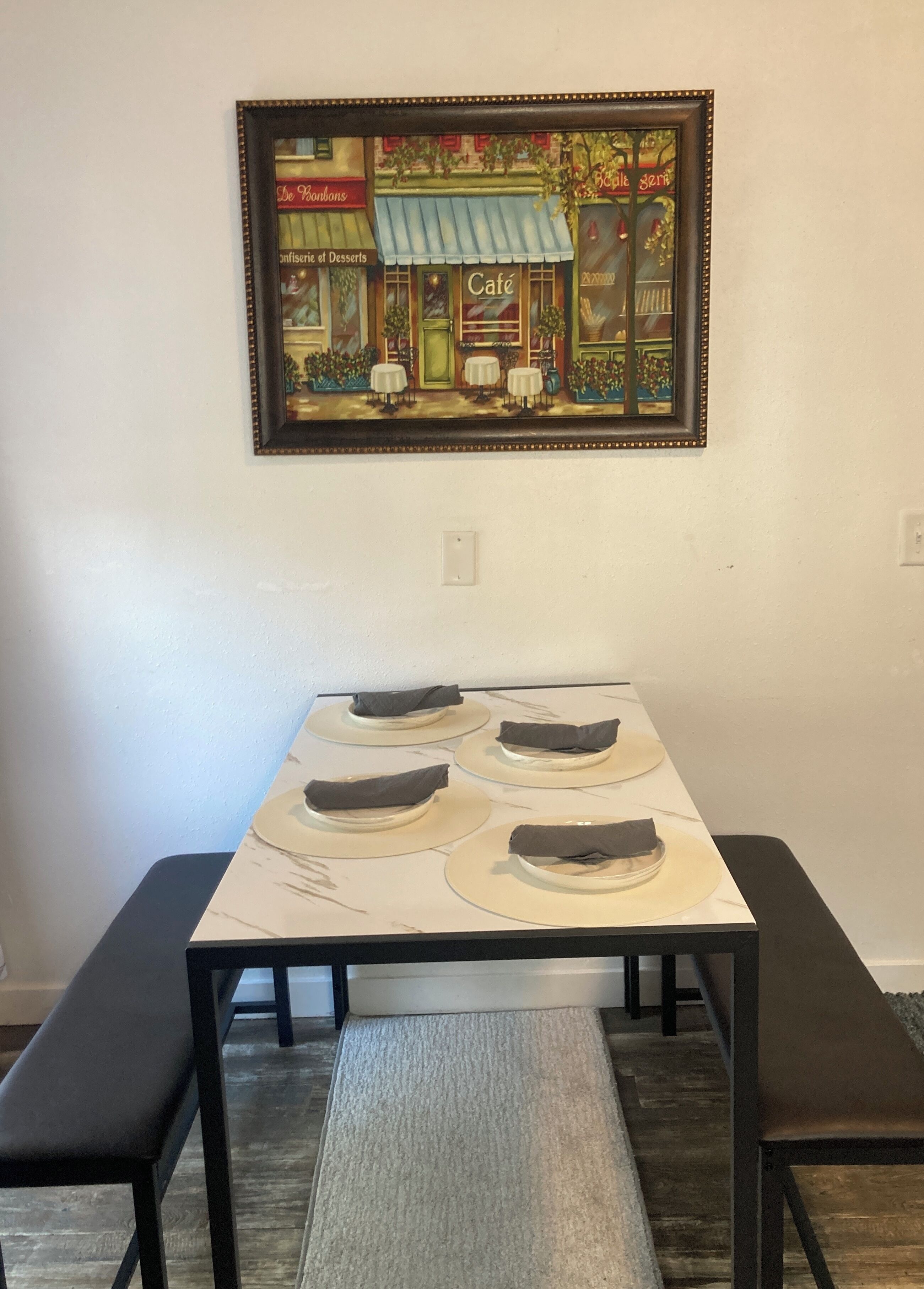 A dining table with four plates, each with a napkin, set on a white tablecloth.