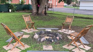 A circular seating arrangement around a fire pit with four wooden chairs and a central fire.