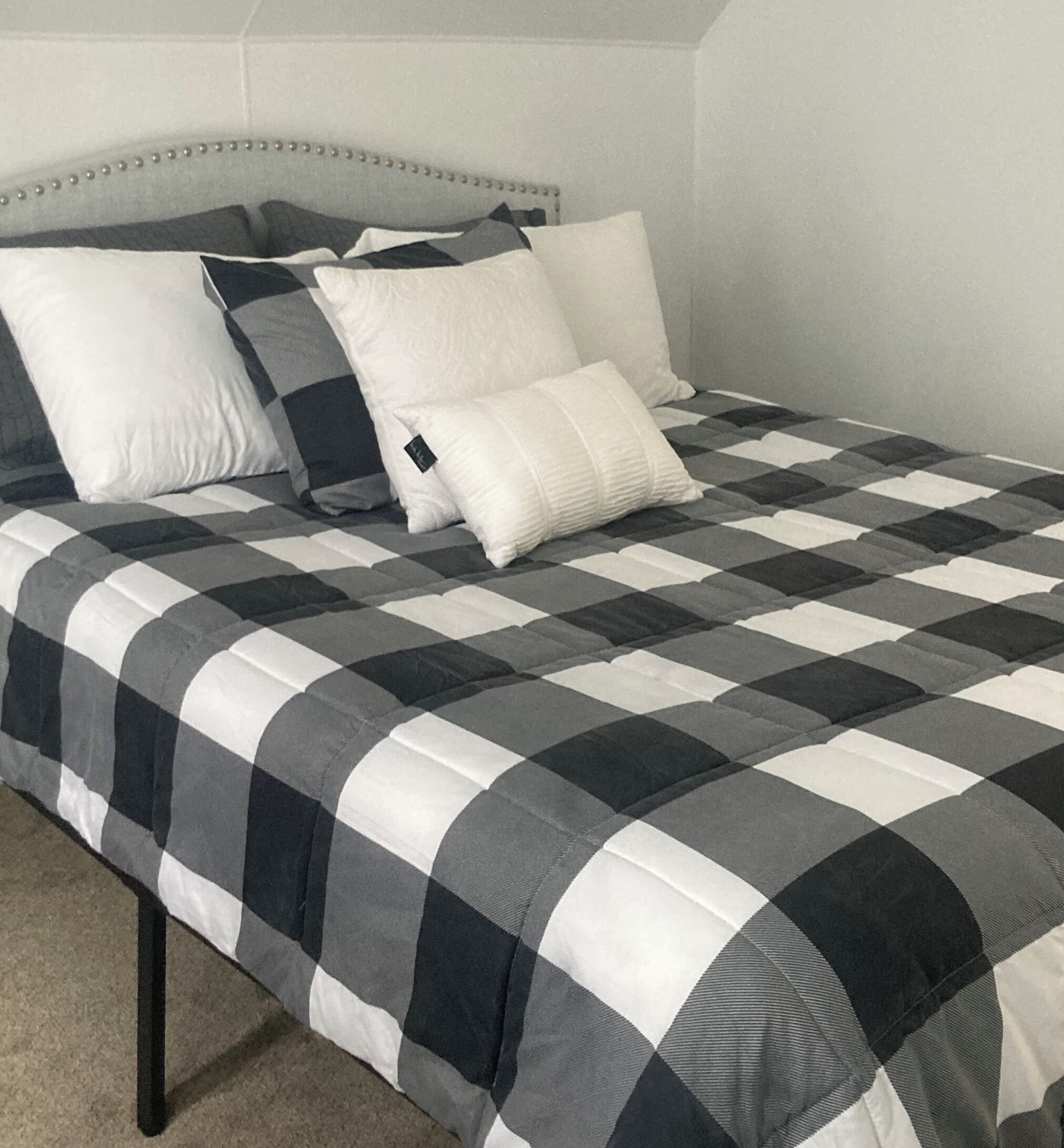 A bed with a checkered bedspread, a headboard, and several pillows.
