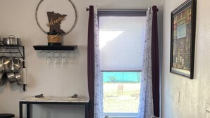A compact kitchen with a dining area, a window with curtains, and a mounted picture.