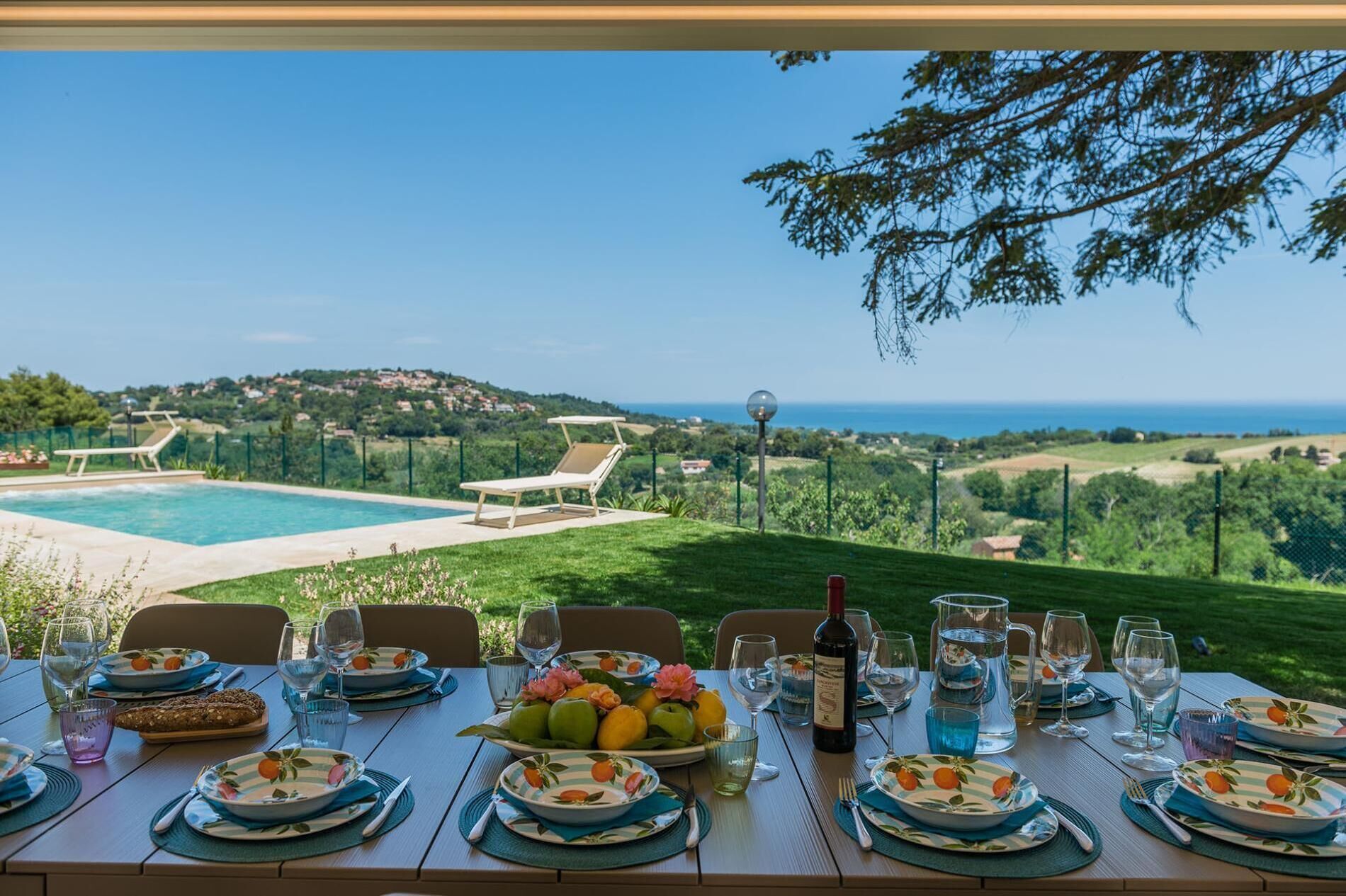 Une table à manger dressée pour un repas, avec vue sur une piscine et la mer.