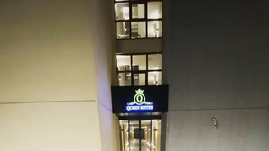 Een hotelentree met een bord waarop 'Queen Suites' staat, een natte stoep en buitenverlichting.