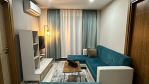 A modern living room with a teal sofa, a white armchair, a wooden coffee table, and a small white cabinet.