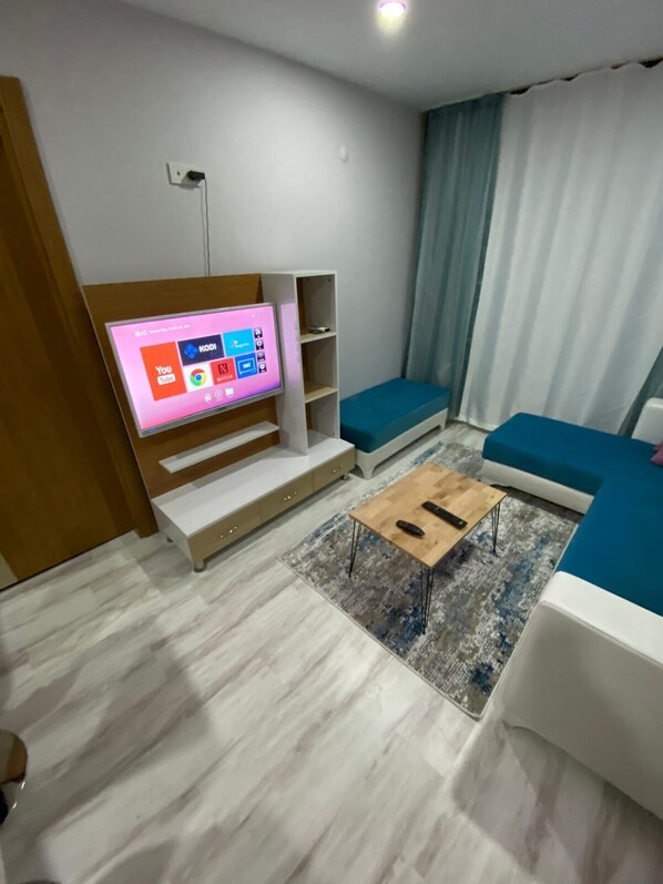 A modern living room with a flat-screen TV, built-in shelves, a wooden coffee table, and blue upholstered seating. - QUEEN SUİTES GÖRÜKLE (Bursa)