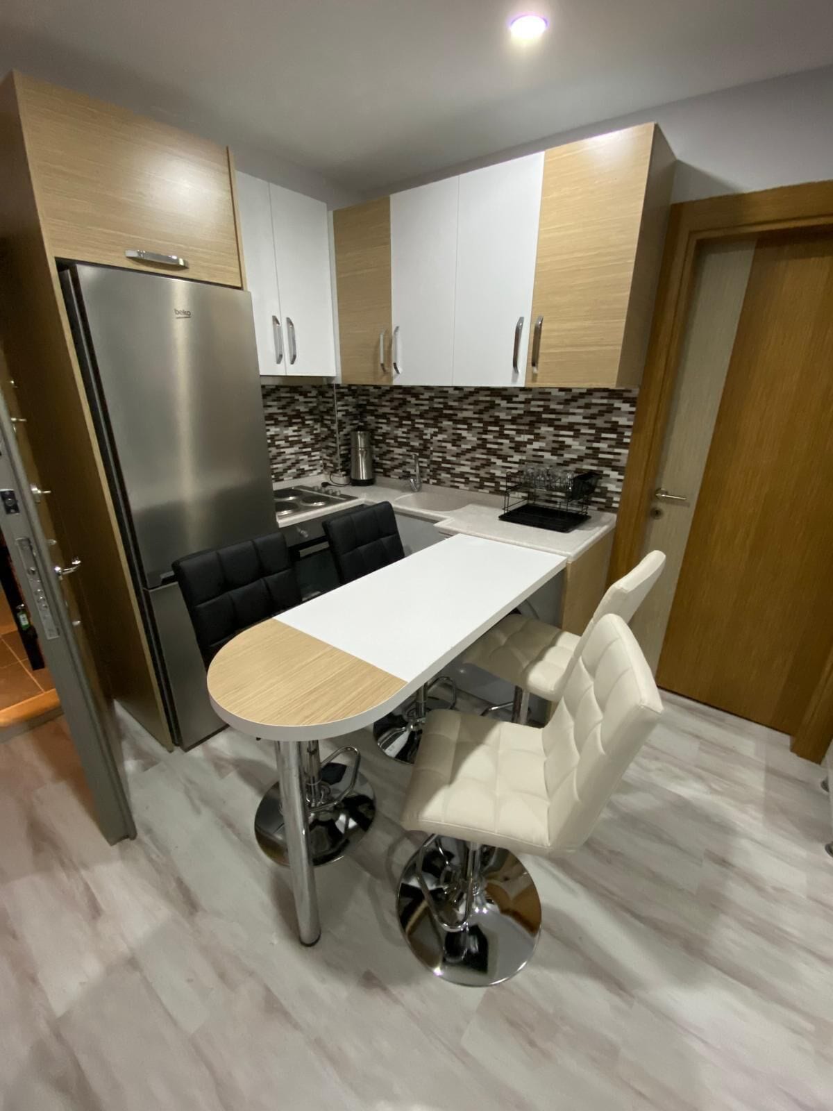 Une cuisine moderne avec un réfrigérateur en acier inoxydable, une table à manger blanche et deux chaises, ainsi qu’un pare-feu en carrelage.