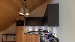 A modern kitchen with wooden cabinets, a black countertop, and a hanging light fixture. - Apartment in Chantemerle Near Serre-chevalier (Saint-Chaffrey)