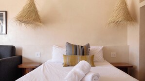 Uma cama bem arrumada com lençóis brancos, duas mesas de cabeceira e uma cadeira.