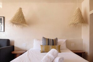 A neatly made bed with white linens, two bedside tables, and a chair. - Cute Studio steps to beach (Imperial Beach)