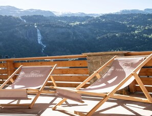 Dos sillones de madera con el logotipo 'TERRESENS' en los cojines, ubicados en una terraza de madera con un paisaje montañoso de fondo.