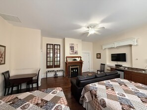 A room with two beds, a dining table, chairs, a fireplace, a television, and a kitchen area. - Lake Huron Lodge (Lexington)
