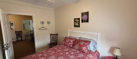 A bedroom with a bed, a ceiling fan, a nightstand, and a door leading to another room.