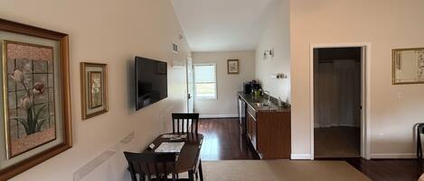 A spacious living room with a dining area, a kitchen, and a hallway leading to a bedroom.