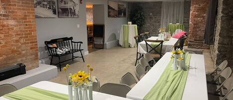 A dining area with tables set for a meal, featuring green tablecloths and white vases with flowers.