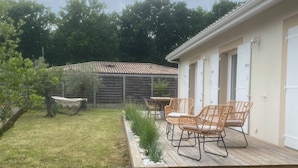 Un patio con sedie in vimini e un tavolo, un pontile in legno e un edificio sullo sfondo con porte numerate.