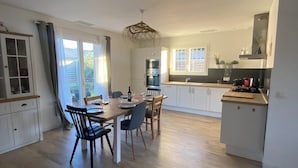 Un'ampia cucina con elettrodomestici moderni, un'area pranzo con tavolo e sedie in legno, e un'ampia finestra che offre luce naturale.