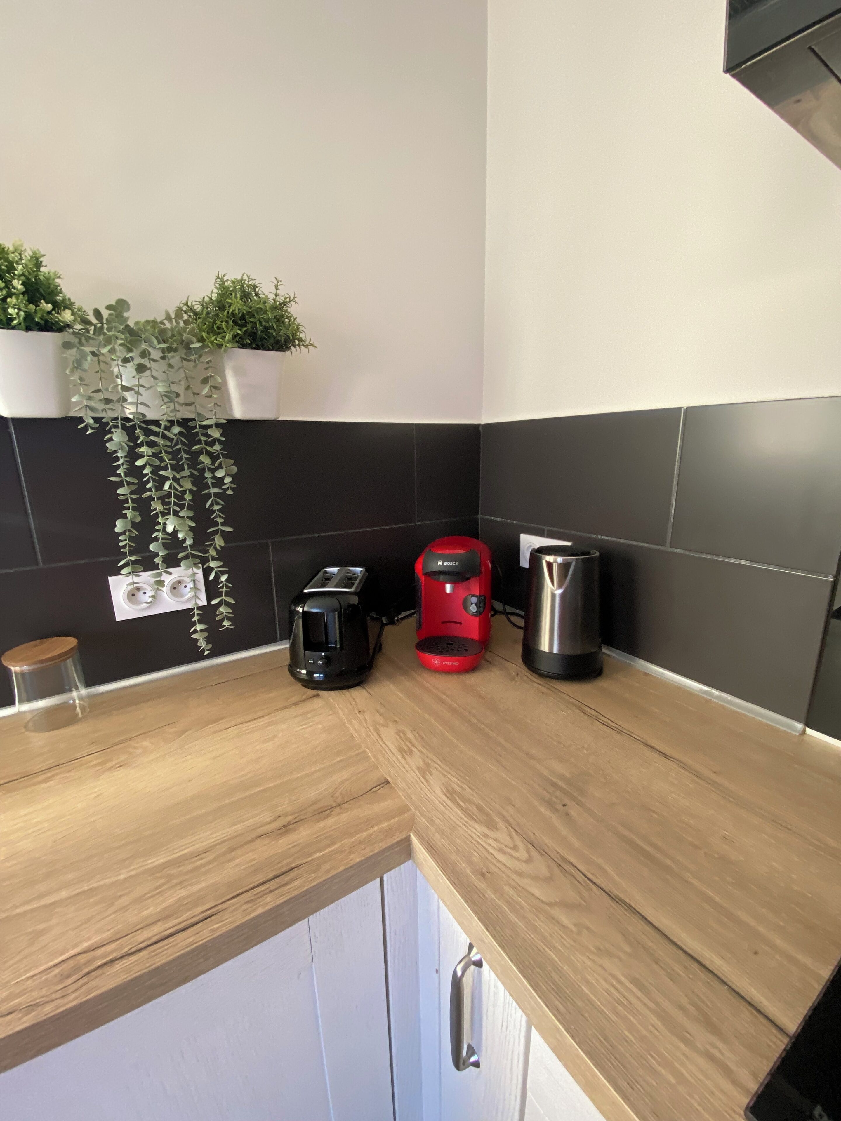 A kitchen with a wooden countertop, a Bosch toaster, a red coffee maker, and a stainless steel kettle.