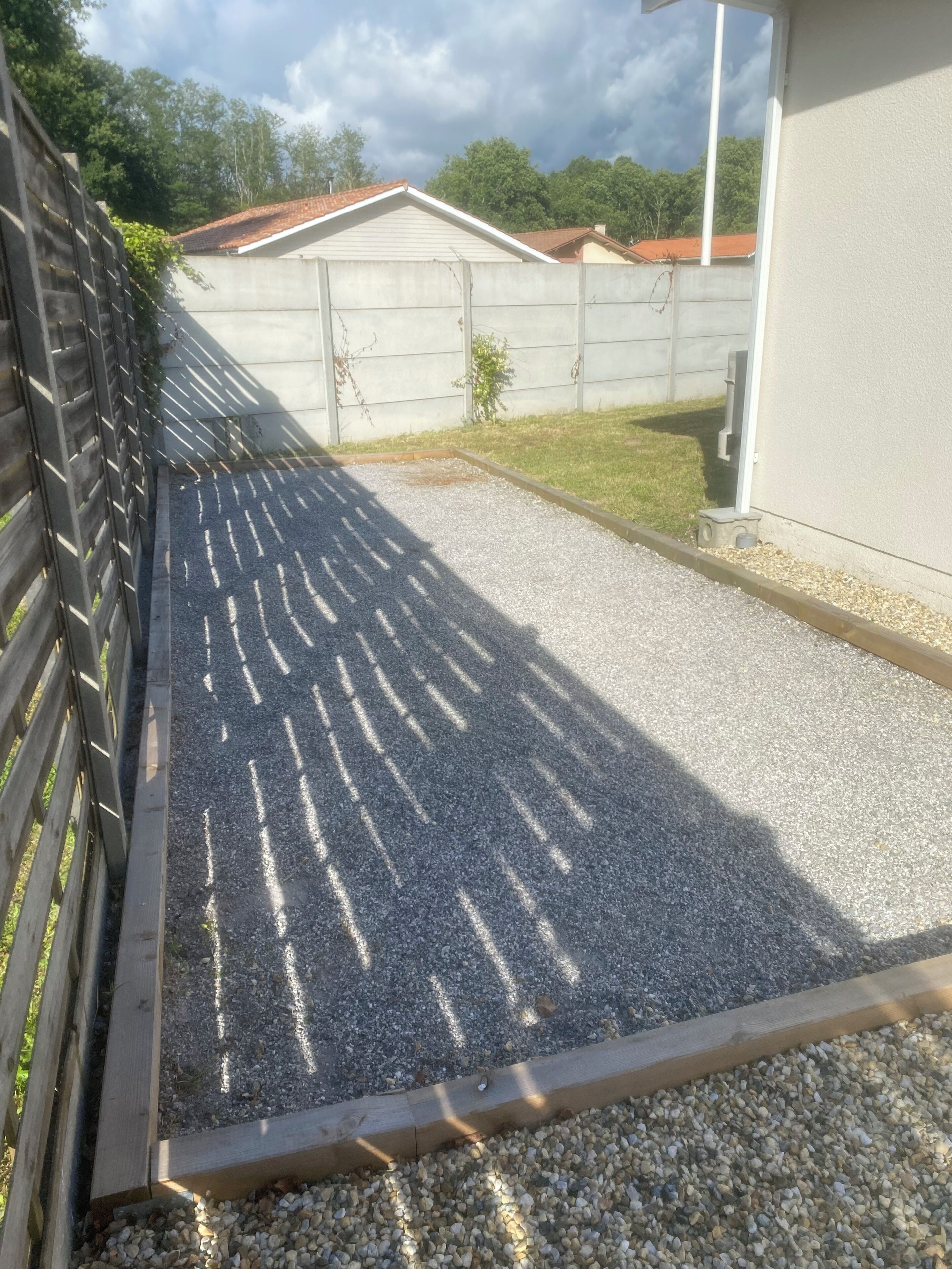 Un camino de grava que conduce a un edificio con un muro de hormigón y una valla metálica.