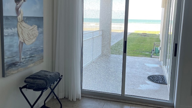 Une pièce décorée d’un tableau représentant une femme au bord de la mer, avec une porte-fenêtre coulissante donnant sur un balcon et une petite table agrémentée d’un coussin.