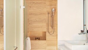 A modern bathroom with a wooden floor, a shower with a handheld showerhead, a sink, and a mirror.