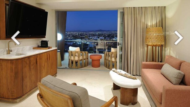 A modern living room with a kitchen area, a sofa, a coffee table, and a TV mounted on the wall.