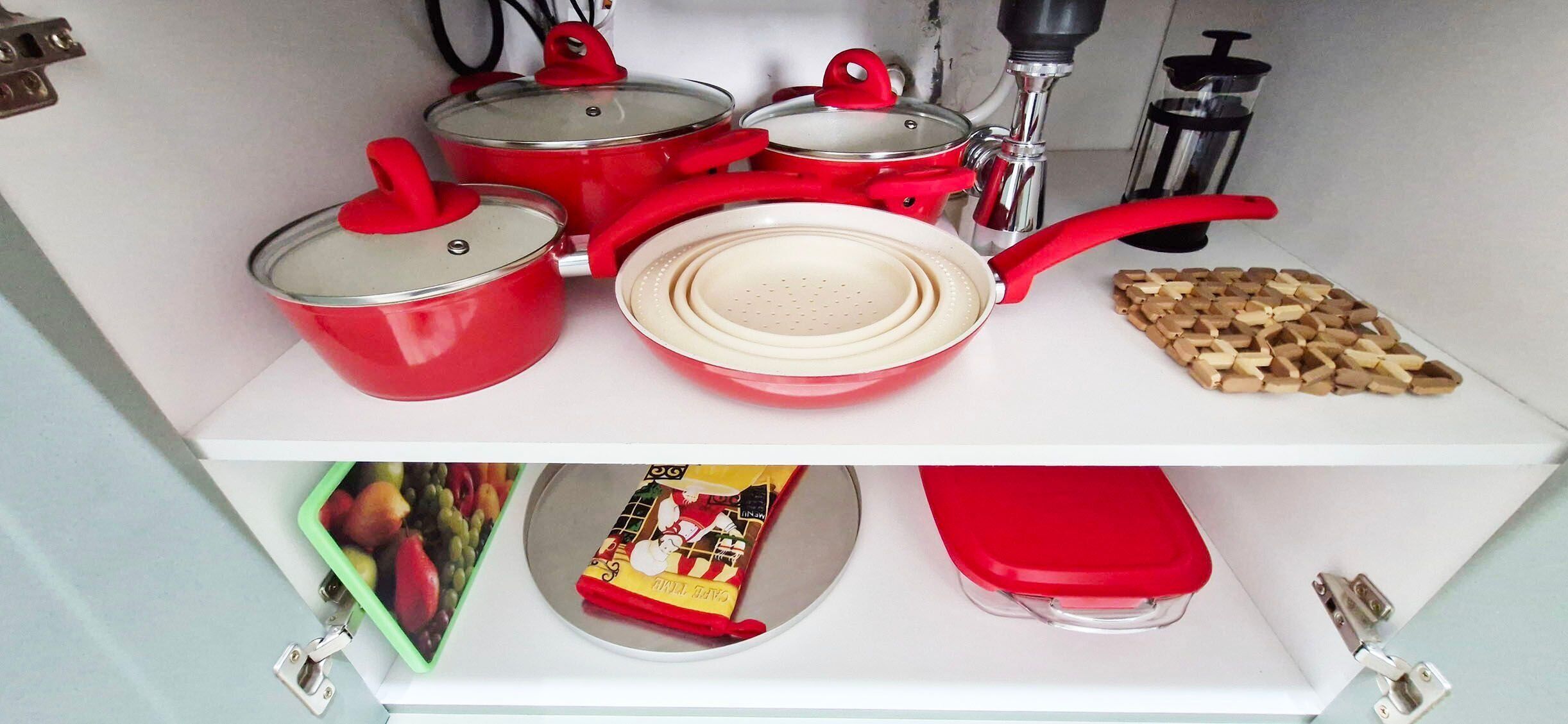 A kitchen with red pots and pans, a colander, wooden utensils, a packet of tea, and a green fruit basket.