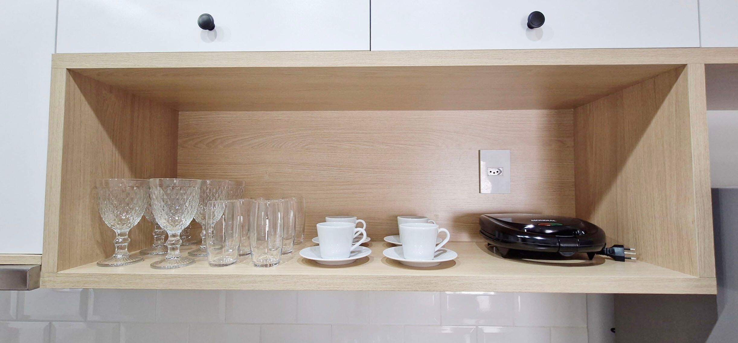 A wooden shelf with glassware, white cups, and a black device.
