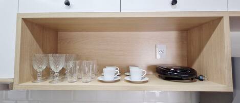 A wooden shelf with glassware, white cups, and a black device.