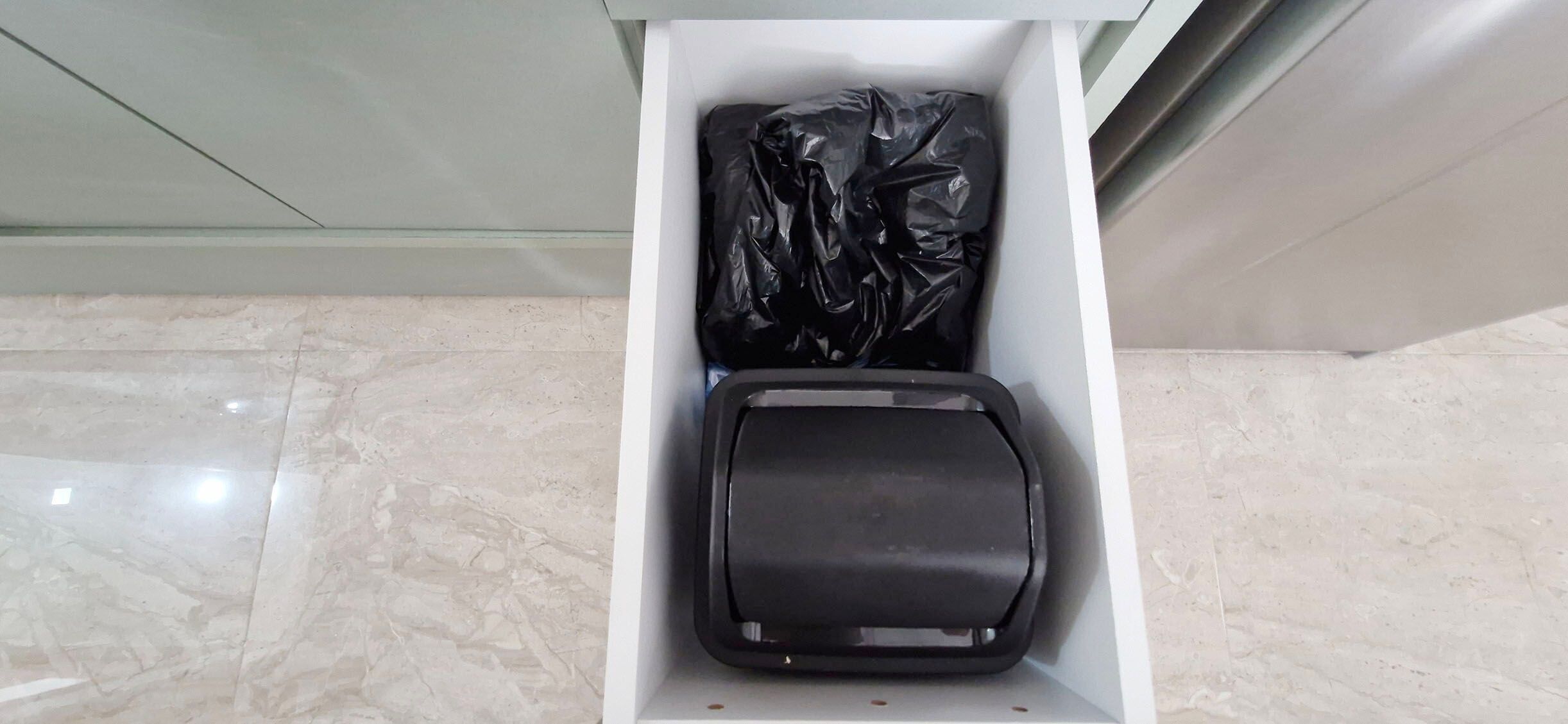A white storage box with a black object and a black plastic bag inside.