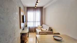 Una sala de estar moderna con un sofá, una mesa de comedor y un televisor instalado en la pared.