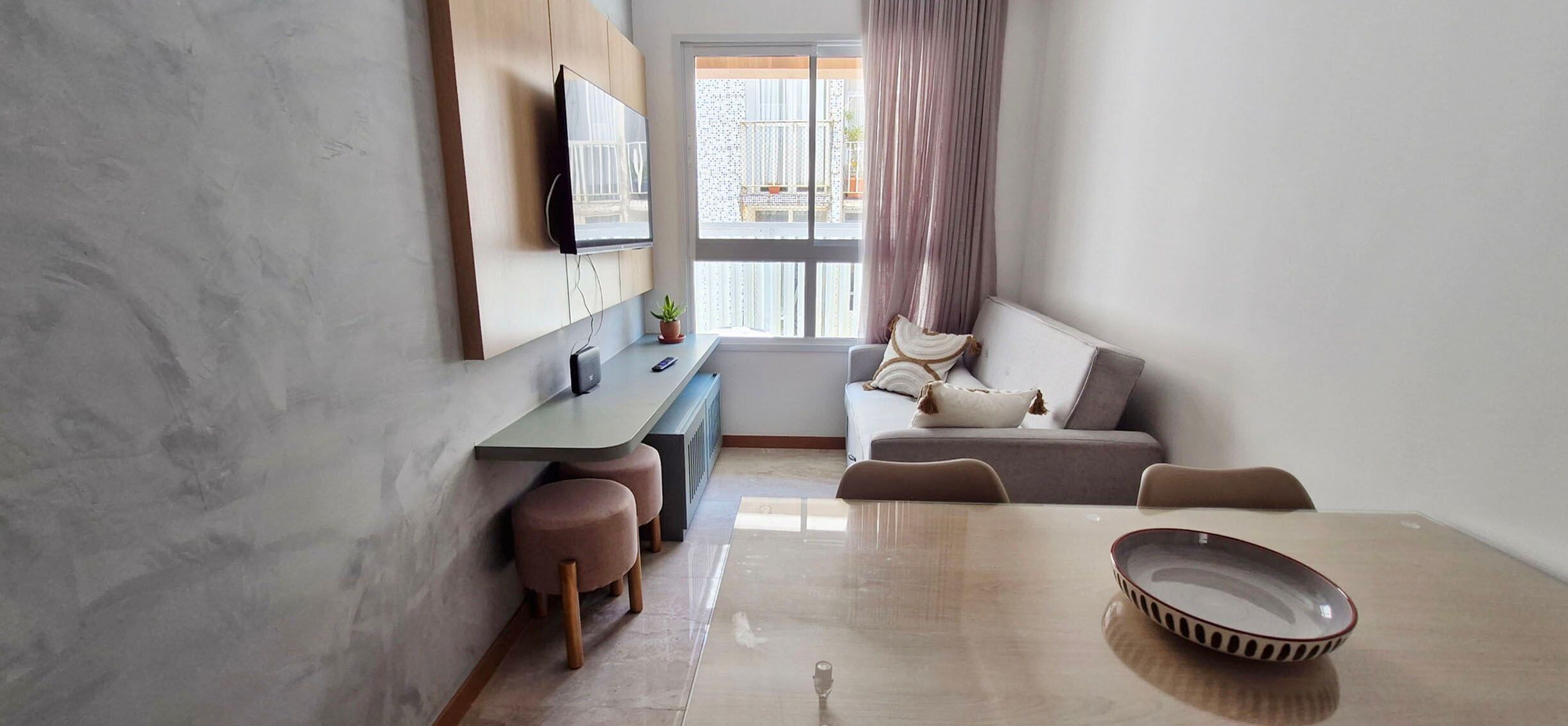 A modern living room with a sofa, a dining table, and a TV mounted on the wall.