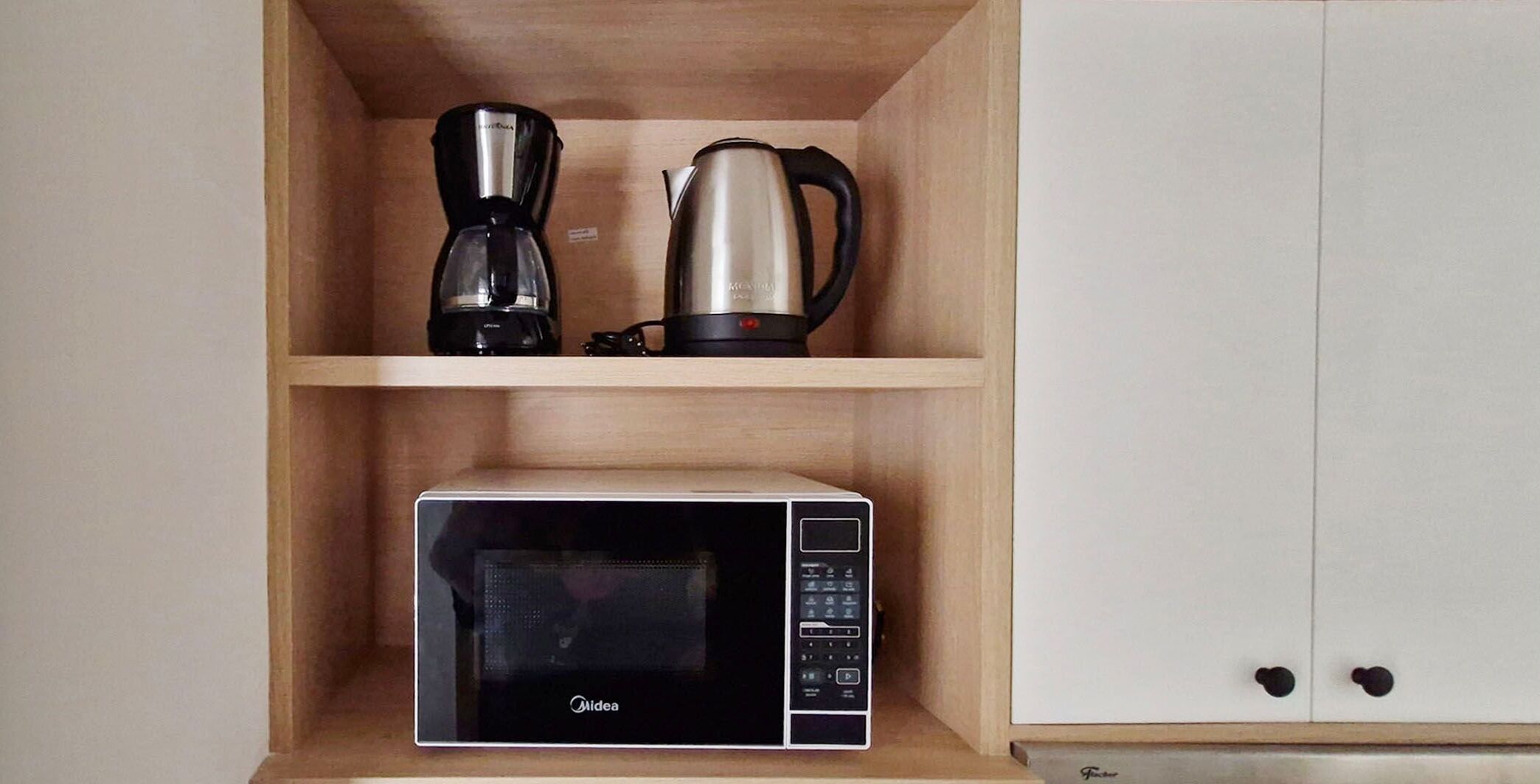 A kitchenette with a coffee maker, a kettle, and a microwave.