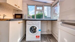 A compact kitchen with a washing machine, a microwave, and a window overlooking a garden. - 3-bedroom apartment in awesome Birmingham with WiFi (Birmingham)