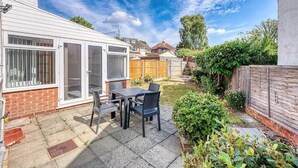A patio with a table and chairs, a wooden fence, and a garden. - 3-bedroom apartment in awesome Birmingham with WiFi (Birmingham)