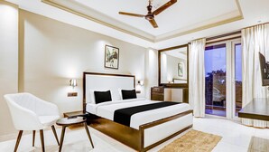 A bedroom with a bed, a chair, a desk, a ceiling fan, and a view through a glass door. - Classic Cloud Bay (Gurugram)