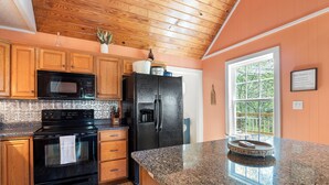 A kitchen with wooden cabinets, a black refrigerator, a microwave, and a stove. - Thistle Brae - Dock Toys galore! And Pet-Friendly! (Houston)