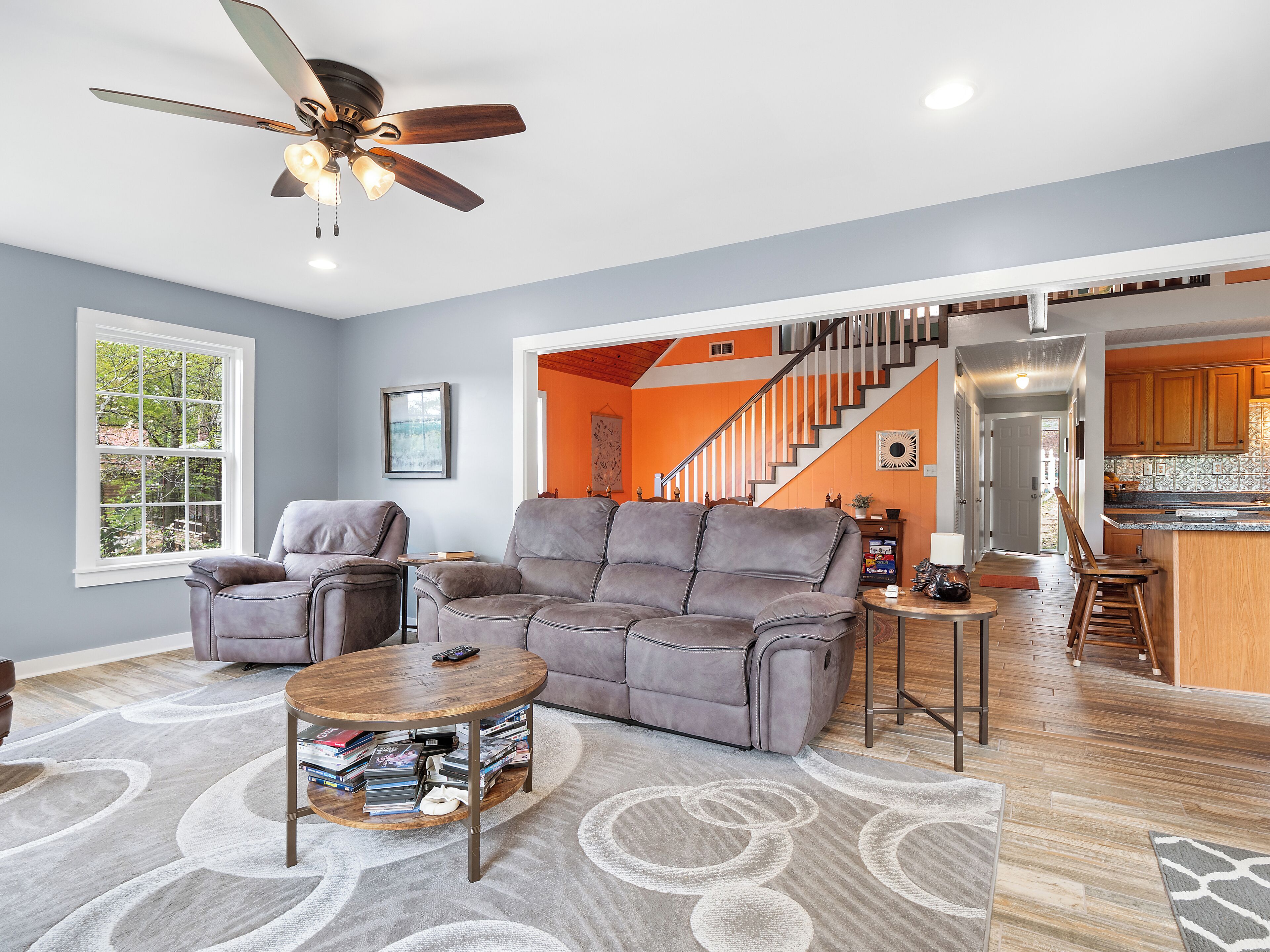 A living room with a grey sectional sofa, a coffee table with books, and a ceiling fan.