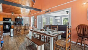 A spacious kitchen with wooden cabinets, a black refrigerator, and a microwave. There is a dining area with a wooden table and chairs, and a living room with a sofa and a television. - Thistle Brae - Dock Toys galore! And Pet-Friendly! (Houston)