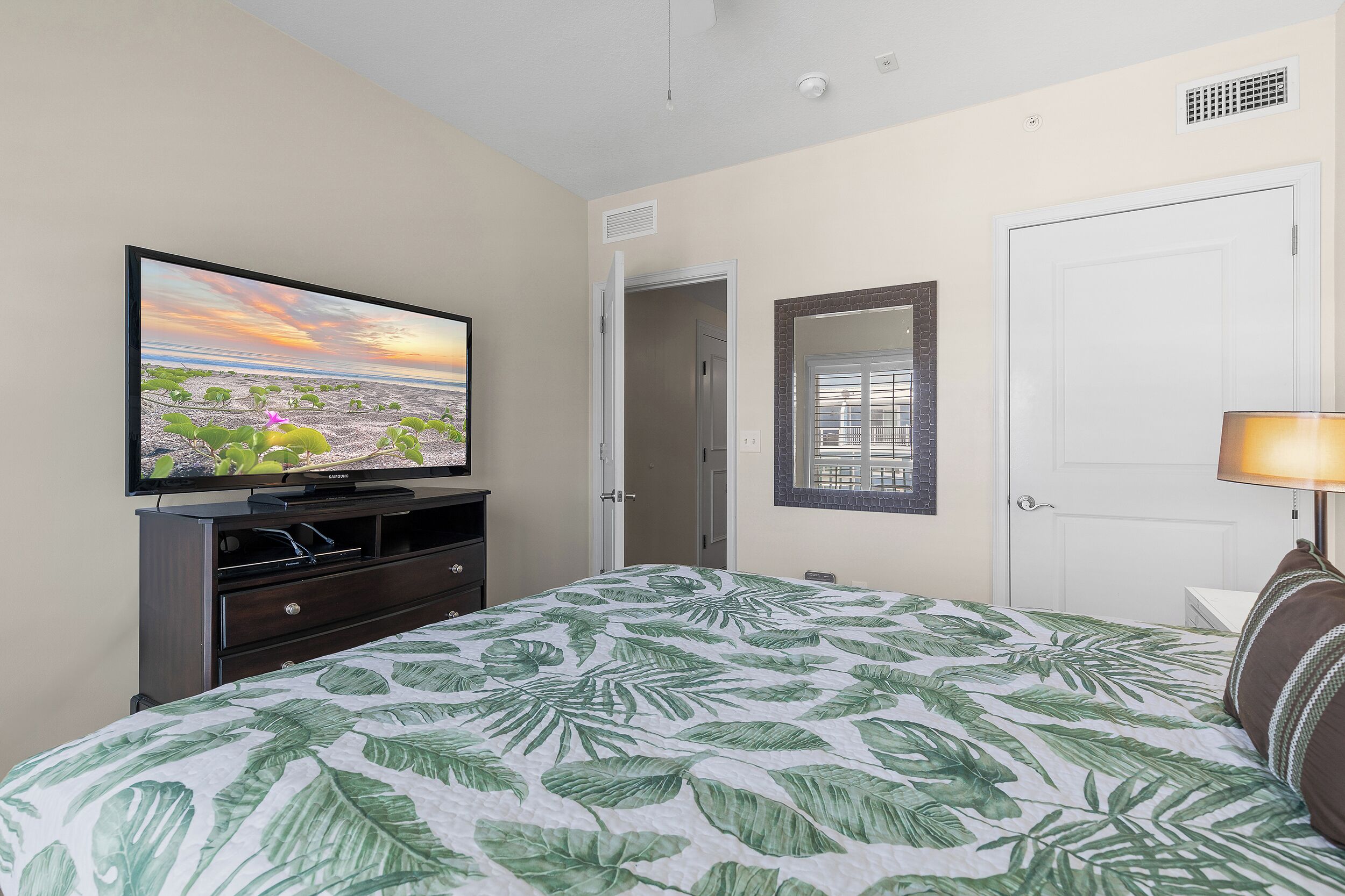 Un dormitorio con cama, televisión sobre un mueble, una puerta y una ventana con persianas.