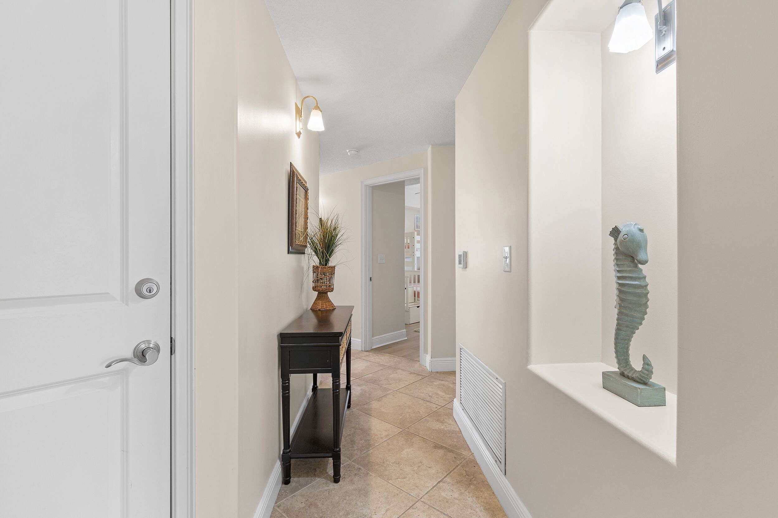 A hallway with a white door, a black console table with a plant, and a sculpture on a shelf.