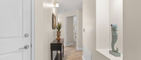 A hallway with a white door, a black console table with a plant, and a sculpture on a shelf.