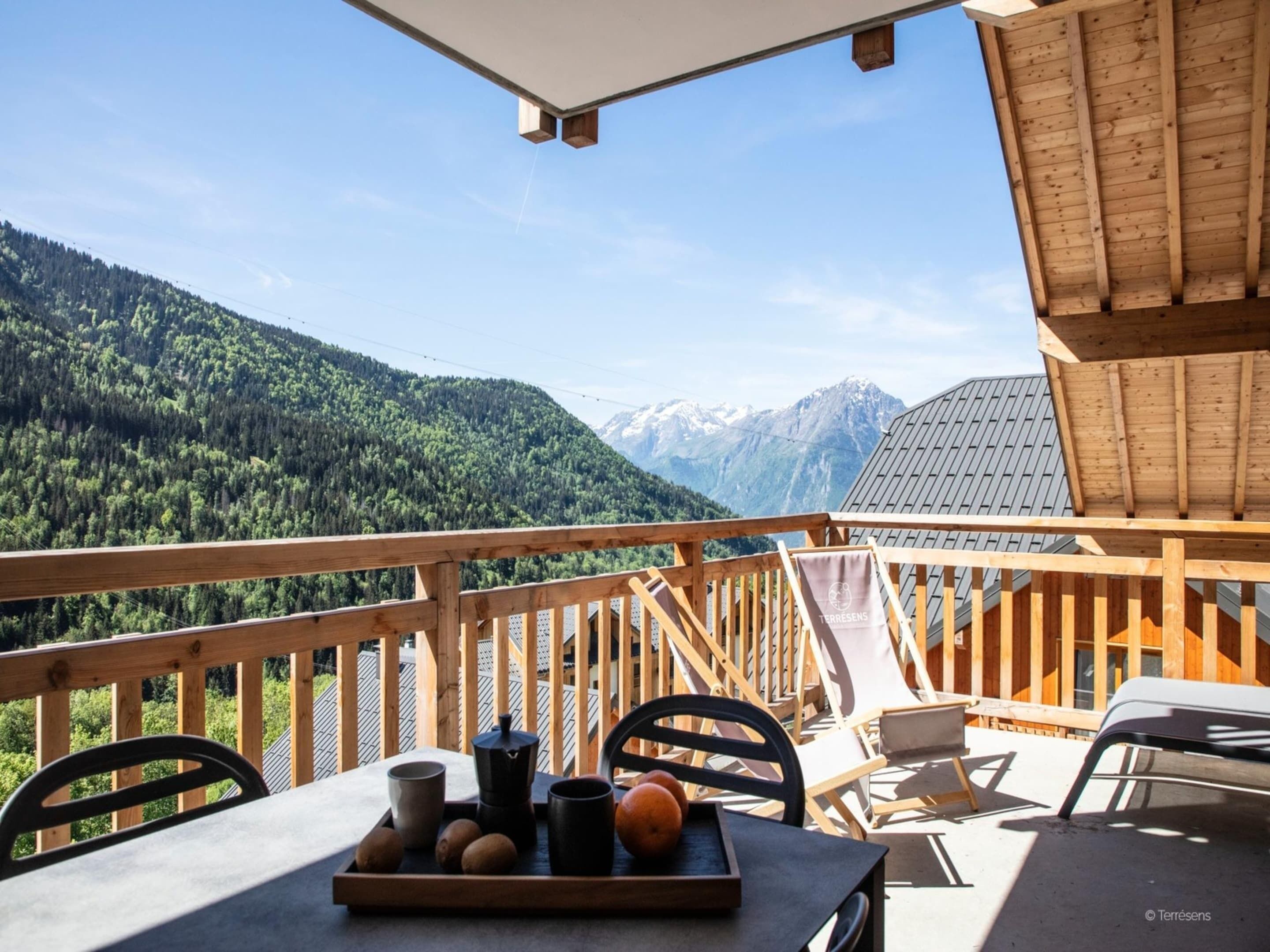 A wooden deck with a table set for breakfast, overlooking a mountainous landscape.